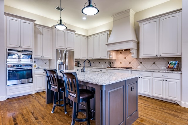 kitchen with white cabinetry, custom exhaust hood, and an island with sink