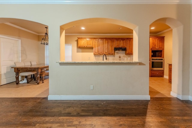 kitchen with ornamental molding, oven, hardwood / wood-style floors, and backsplash