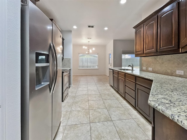 kitchen with sink, hanging light fixtures, stainless steel appliances, light stone countertops, and dark brown cabinets