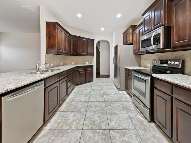 kitchen with stainless steel appliances, light tile patterned flooring, dark brown cabinets, and sink