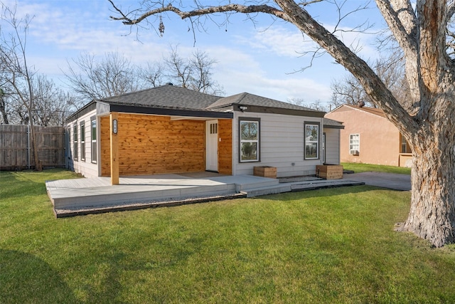 rear view of property with a shingled roof, fence, and a yard