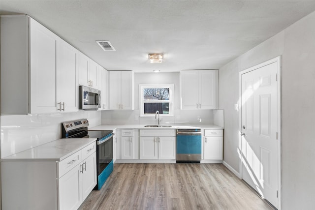 kitchen featuring white cabinetry, stainless steel appliances, sink, and light wood-type flooring