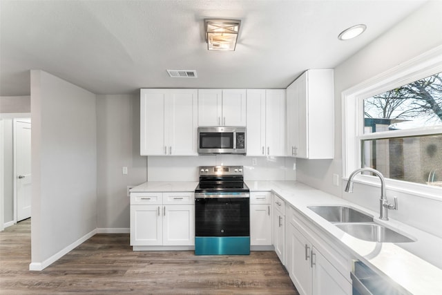 kitchen featuring hardwood / wood-style flooring, appliances with stainless steel finishes, sink, and white cabinets