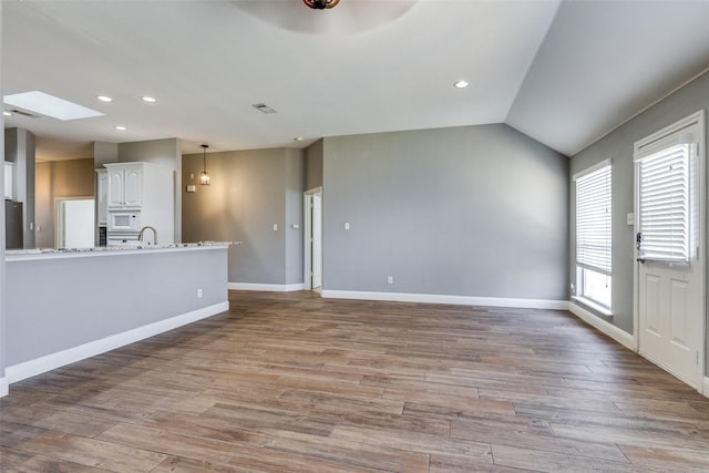 unfurnished living room featuring light hardwood / wood-style flooring and vaulted ceiling with skylight