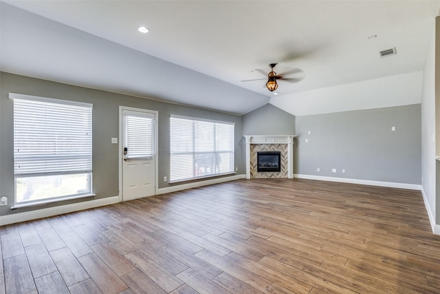 unfurnished living room featuring a tiled fireplace, vaulted ceiling, ceiling fan, and light hardwood / wood-style flooring