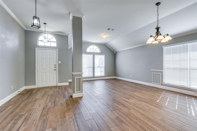 foyer entrance featuring lofted ceiling, decorative columns, ornamental molding, a chandelier, and light wood-type flooring