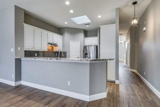 kitchen featuring a skylight, white cabinetry, stainless steel fridge, light stone counters, and kitchen peninsula