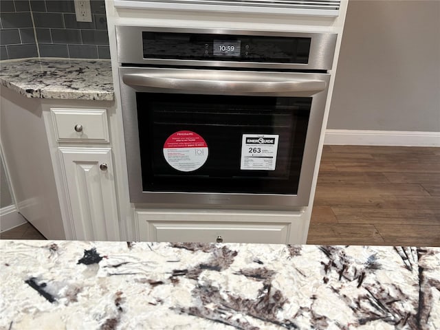 room details featuring white cabinetry, oven, backsplash, dark hardwood / wood-style flooring, and light stone countertops