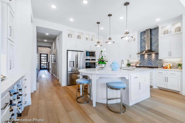 kitchen with stainless steel appliances, pendant lighting, white cabinets, and wall chimney exhaust hood