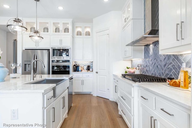 kitchen with white cabinets, hanging light fixtures, stainless steel appliances, light stone countertops, and wall chimney exhaust hood