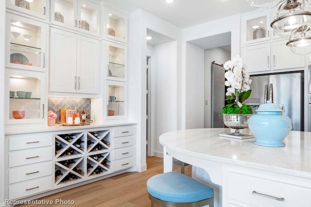 bar featuring white cabinetry, backsplash, hanging light fixtures, light stone counters, and light hardwood / wood-style flooring