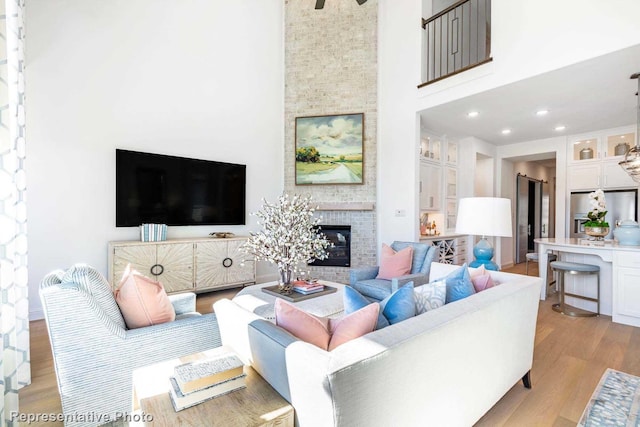 living room featuring light wood-type flooring, a fireplace, and a towering ceiling