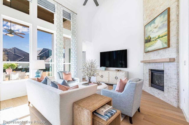 living room featuring a high ceiling, light wood-type flooring, a fireplace, and ceiling fan