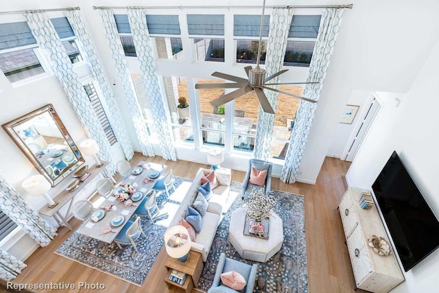 living room with a high ceiling, ceiling fan, and light wood-type flooring