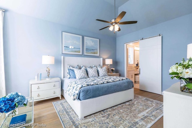 bedroom featuring ceiling fan, ensuite bath, wood-type flooring, and a barn door