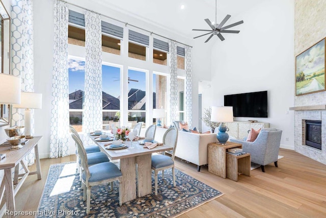 interior space with ceiling fan, a fireplace, light hardwood / wood-style floors, and a towering ceiling