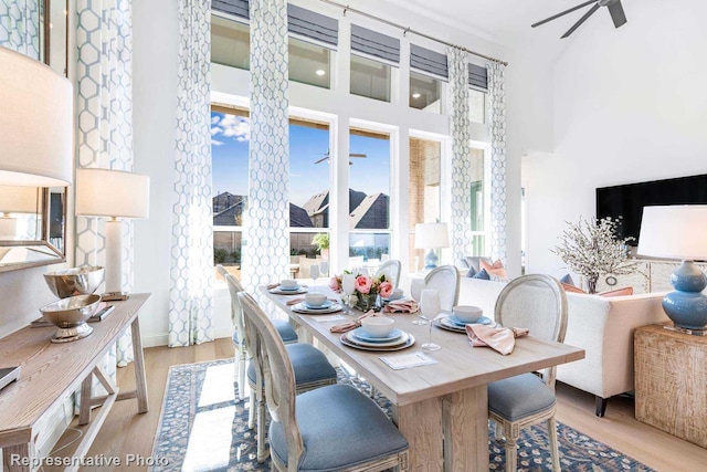 dining area with a towering ceiling, ceiling fan, and light hardwood / wood-style flooring