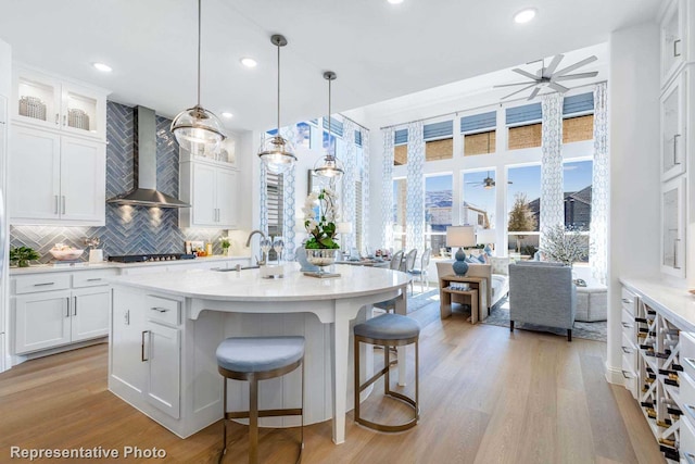 kitchen featuring white cabinetry, pendant lighting, ceiling fan, and wall chimney exhaust hood