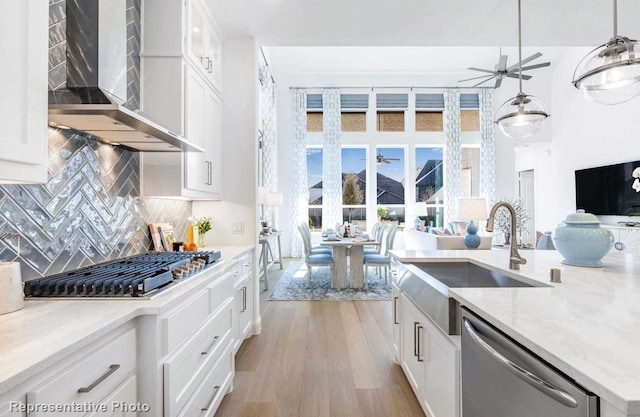 kitchen with appliances with stainless steel finishes, white cabinets, hanging light fixtures, ceiling fan, and wall chimney range hood