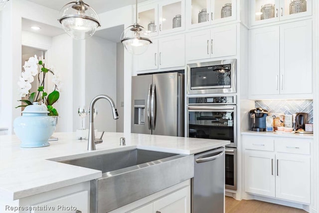 kitchen featuring light stone countertops, white cabinetry, appliances with stainless steel finishes, and decorative light fixtures