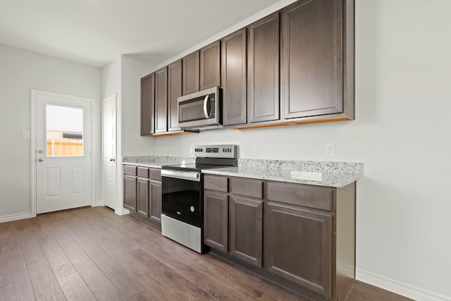 kitchen featuring dark wood finished floors, baseboards, stainless steel appliances, and dark brown cabinets