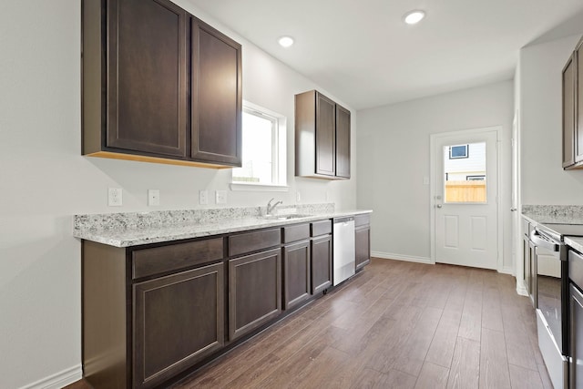 kitchen featuring appliances with stainless steel finishes, dark wood-type flooring, a sink, dark brown cabinetry, and light stone countertops