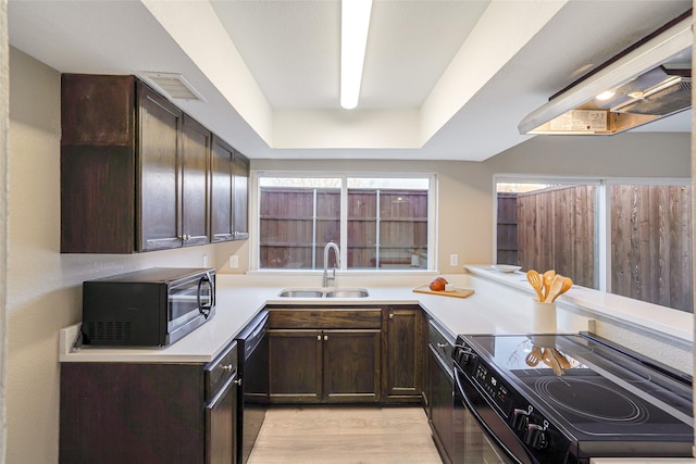 kitchen with dark brown cabinetry, sink, light hardwood / wood-style flooring, a raised ceiling, and black appliances