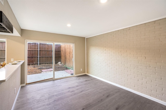 unfurnished room featuring hardwood / wood-style flooring and brick wall