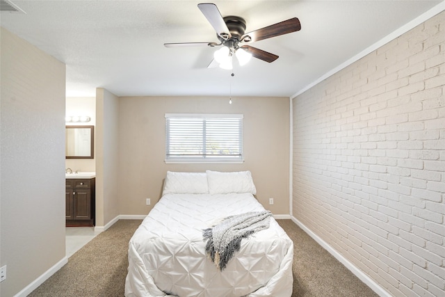 carpeted bedroom with ensuite bath, ceiling fan, and brick wall