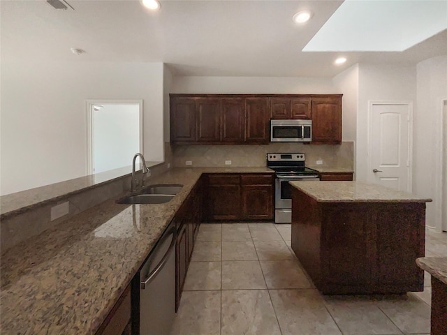 kitchen featuring light stone counters, sink, a skylight, and appliances with stainless steel finishes