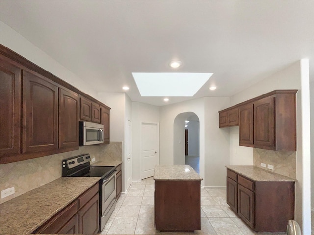 kitchen featuring light stone counters, a center island, dark brown cabinets, appliances with stainless steel finishes, and decorative backsplash