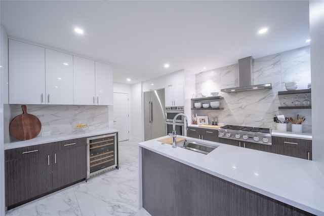 kitchen featuring appliances with stainless steel finishes, white cabinetry, sink, beverage cooler, and wall chimney range hood