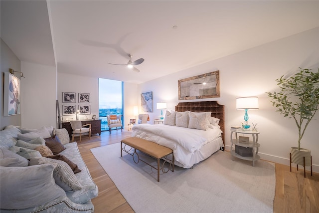 bedroom with light wood finished floors, baseboards, a wall of windows, and a ceiling fan