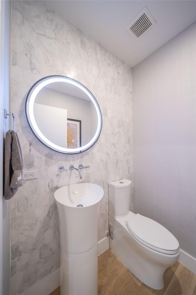 half bathroom with visible vents, toilet, and wood finished floors