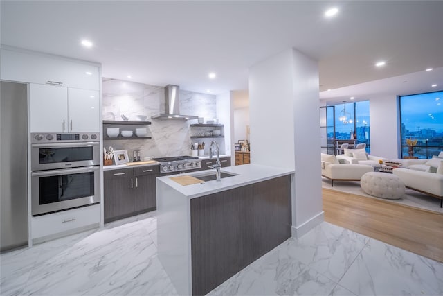 kitchen featuring wall chimney range hood, sink, white cabinetry, stainless steel appliances, and decorative backsplash