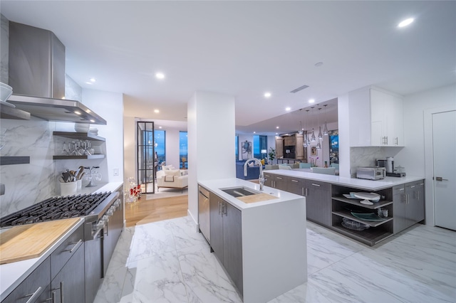 kitchen with sink, white cabinetry, an island with sink, range hood, and decorative backsplash