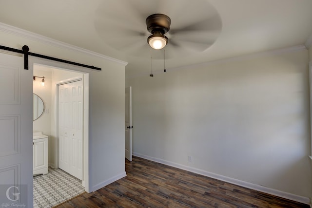 unfurnished bedroom featuring ornamental molding, a barn door, dark hardwood / wood-style floors, and a closet