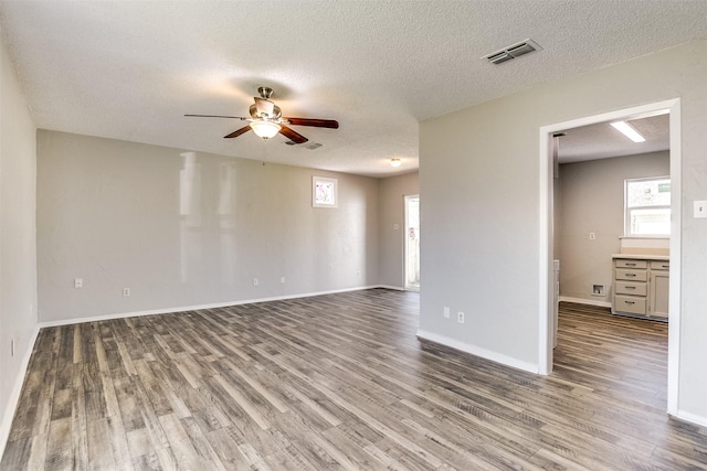 unfurnished living room featuring baseboards, visible vents, ceiling fan, and dark wood-style flooring