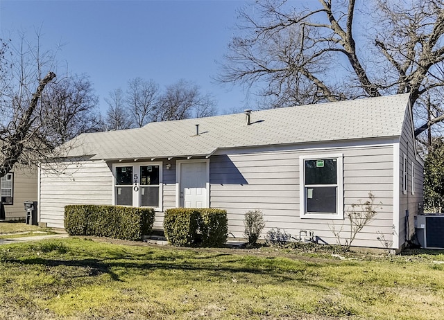 ranch-style house featuring a front lawn, cooling unit, and roof with shingles