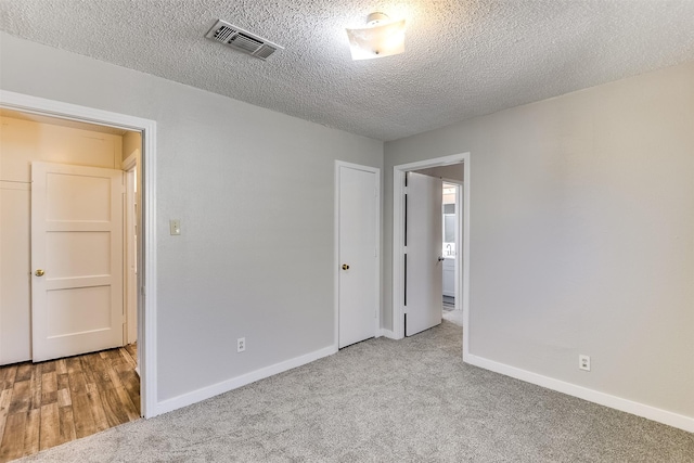 unfurnished bedroom with light carpet, baseboards, visible vents, and a textured ceiling