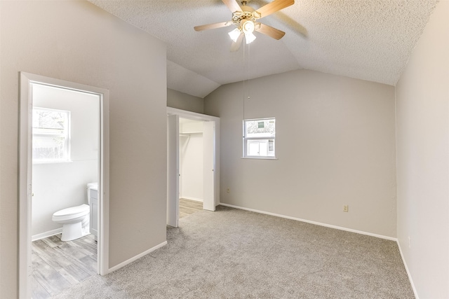 unfurnished bedroom featuring light carpet, baseboards, ensuite bath, vaulted ceiling, and a textured ceiling