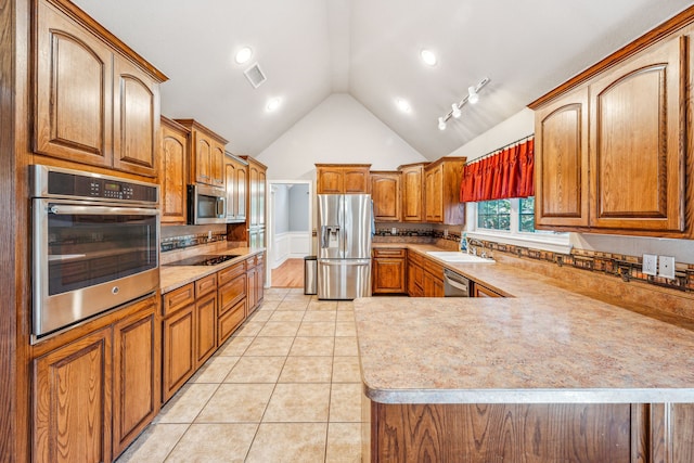 kitchen featuring sink, light tile patterned floors, stainless steel appliances, vaulted ceiling, and kitchen peninsula