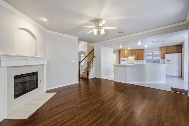 unfurnished living room with crown molding, ceiling fan, a fireplace, and light wood-type flooring