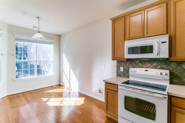 kitchen with white appliances, light hardwood / wood-style floors, hanging light fixtures, and backsplash