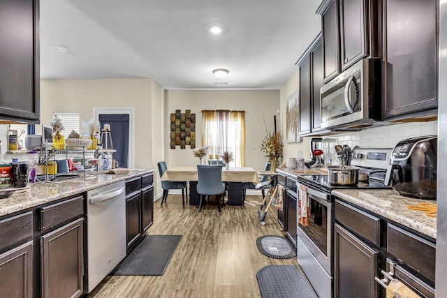 kitchen featuring light hardwood / wood-style flooring, stainless steel appliances, dark brown cabinetry, light stone countertops, and decorative backsplash