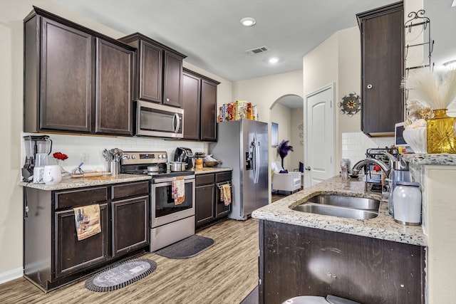 kitchen with dark brown cabinetry, appliances with stainless steel finishes, light stone countertops, and sink