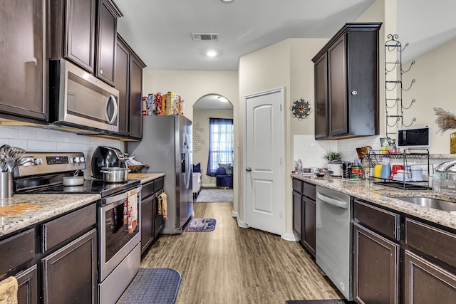 kitchen featuring sink, light hardwood / wood-style flooring, dark brown cabinets, stainless steel appliances, and light stone counters