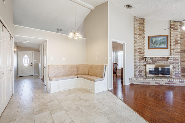 bathroom featuring wood-type flooring, a chandelier, high vaulted ceiling, a brick fireplace, and a textured ceiling