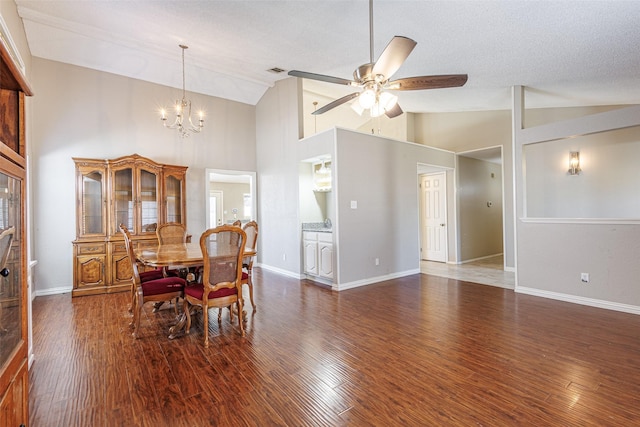 dining area with dark wood-type flooring, high vaulted ceiling, ceiling fan with notable chandelier, and a textured ceiling