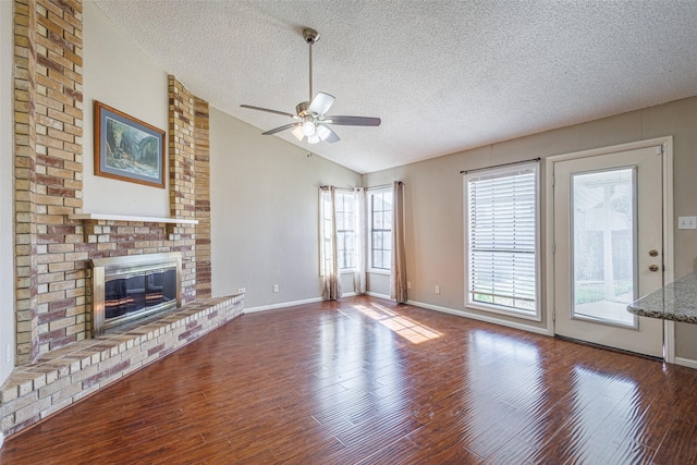 unfurnished living room featuring lofted ceiling, hardwood / wood-style flooring, ceiling fan, a brick fireplace, and a textured ceiling